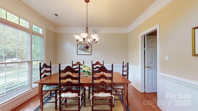 dining room featuring a wainscoted wall, wood finished floors, a chandelier, and ornamental molding
