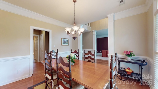 dining area featuring a wainscoted wall, visible vents, a chandelier, wood finished floors, and ornamental molding