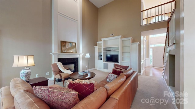 living area featuring a high end fireplace, baseboards, a high ceiling, and light colored carpet