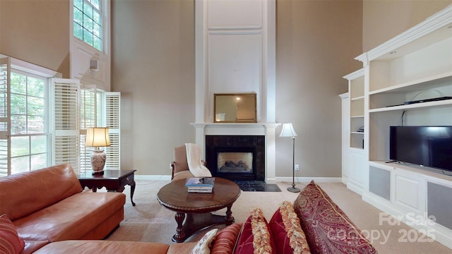 living area with light carpet, baseboards, a high ceiling, and a fireplace