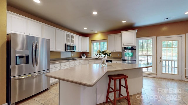 kitchen with a center island, light tile patterned floors, stainless steel appliances, white cabinets, and recessed lighting