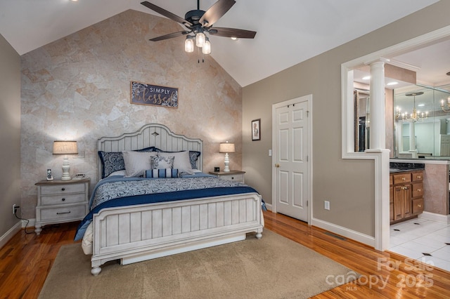 bedroom featuring baseboards, vaulted ceiling, light wood finished floors, decorative columns, and an accent wall