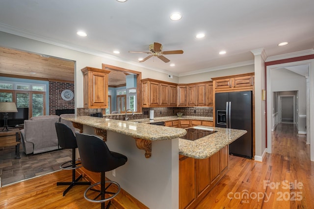 kitchen featuring black appliances, a breakfast bar area, brown cabinets, light stone counters, and recessed lighting