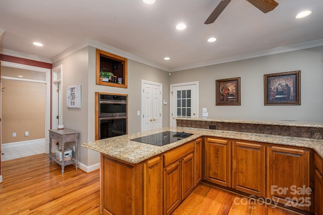 kitchen featuring black electric cooktop, stainless steel double oven, ceiling fan, brown cabinets, and light wood finished floors