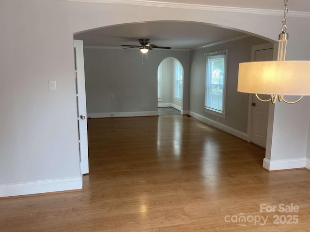 spare room with crown molding, wood finished floors, ceiling fan, arched walkways, and baseboards