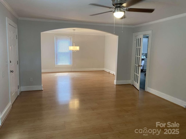 spare room with arched walkways, baseboards, a ceiling fan, wood finished floors, and crown molding