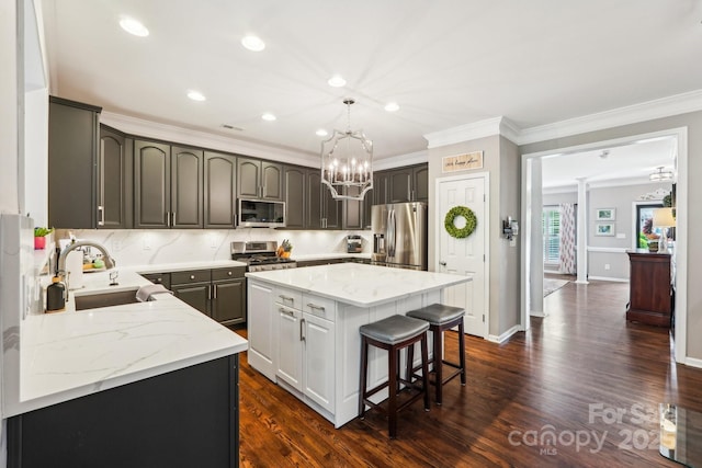 kitchen with a sink, crown molding, a center island, appliances with stainless steel finishes, and a notable chandelier