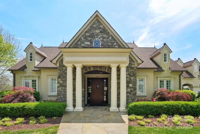 view of front of house featuring stone siding, stucco siding, and a shingled roof