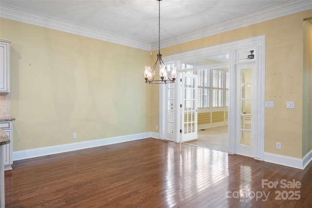 unfurnished dining area featuring wood-type flooring, baseboards, crown molding, and a chandelier