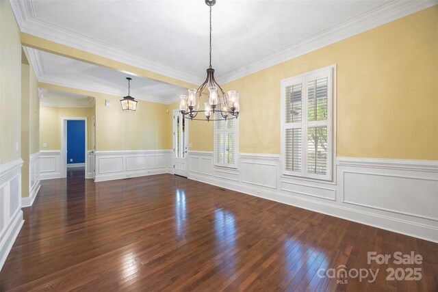 unfurnished dining area with a wainscoted wall, a notable chandelier, ornamental molding, and dark wood finished floors