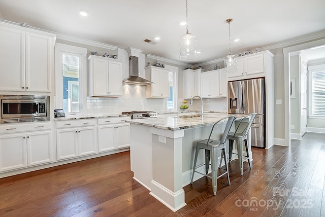 kitchen with stainless steel appliances, visible vents, wall chimney range hood, a sink, and a kitchen bar