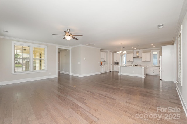 unfurnished living room featuring ceiling fan with notable chandelier, baseboards, a wealth of natural light, and dark wood finished floors