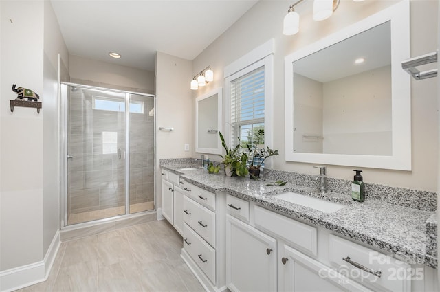 bathroom with baseboards, double vanity, a stall shower, and a sink