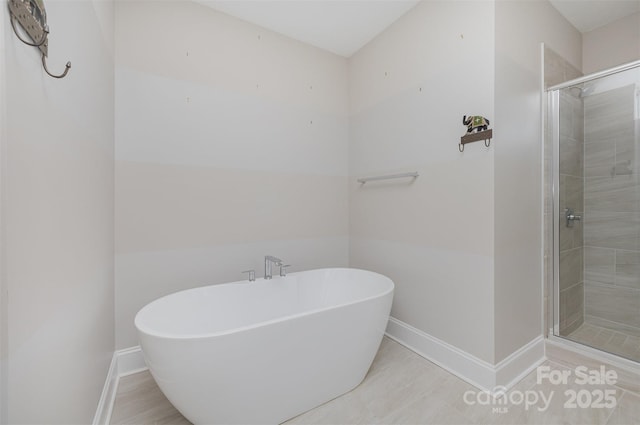 full bath featuring a shower stall, a freestanding bath, and baseboards