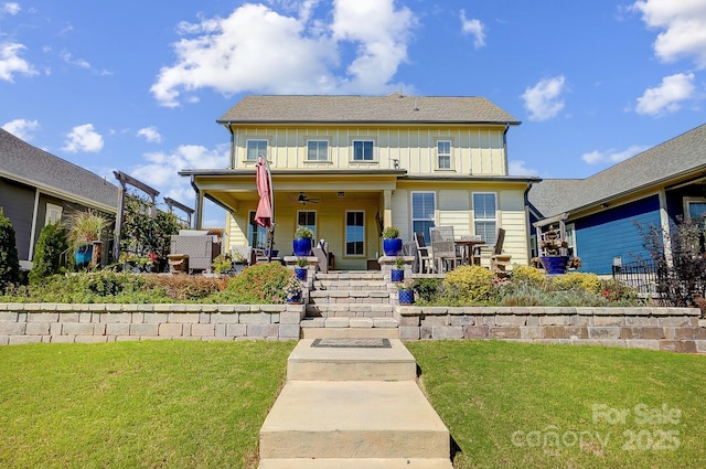 view of front of house with board and batten siding, a patio, a front yard, and ceiling fan