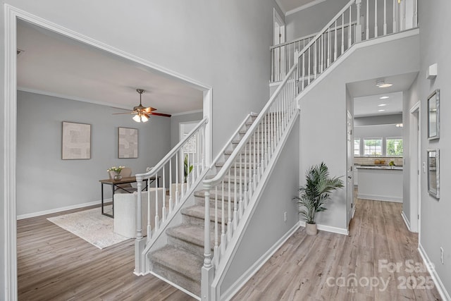 stairs with wood finished floors, a towering ceiling, baseboards, and ceiling fan