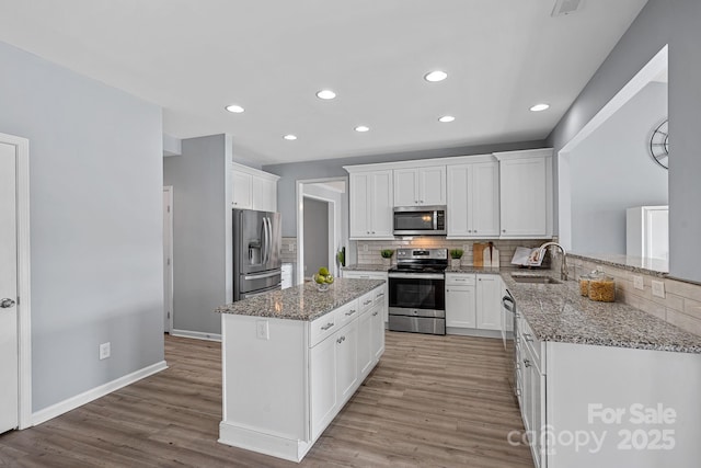 kitchen featuring white cabinets, light wood finished floors, a sink, a kitchen island, and appliances with stainless steel finishes