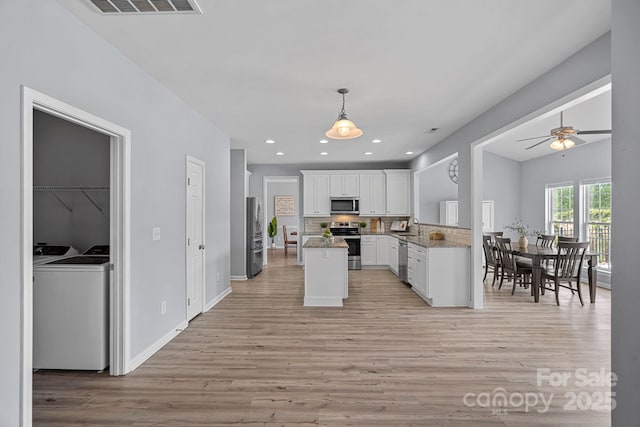 kitchen featuring washing machine and dryer, light wood-type flooring, white cabinets, and stainless steel appliances