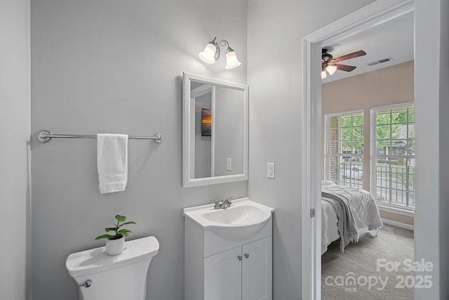 half bath with connected bathroom, vanity, ceiling fan, toilet, and visible vents