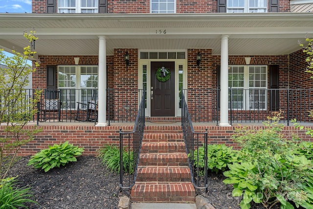 view of exterior entry with brick siding and a porch
