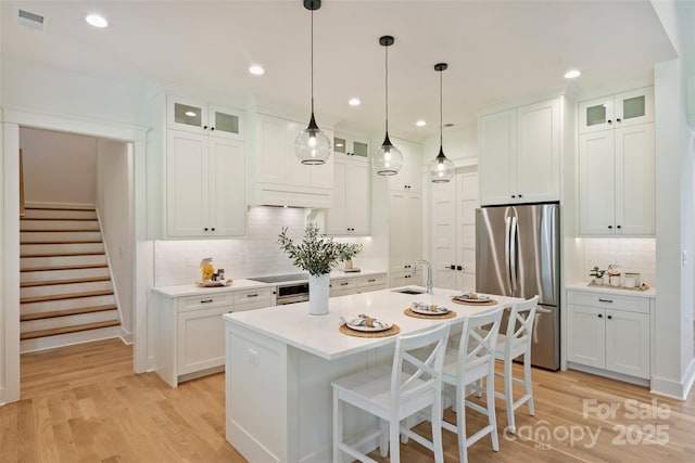 kitchen with tasteful backsplash, freestanding refrigerator, light wood finished floors, a sink, and visible vents
