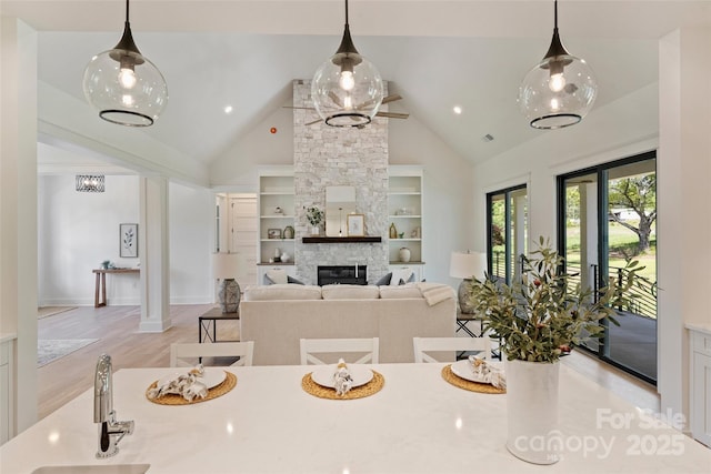 dining area featuring light wood-style floors, built in shelves, a fireplace, high vaulted ceiling, and baseboards