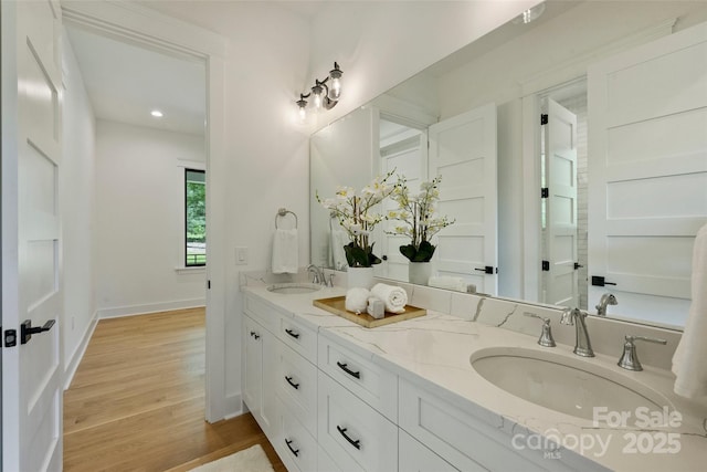 full bathroom with double vanity, wood finished floors, baseboards, and a sink