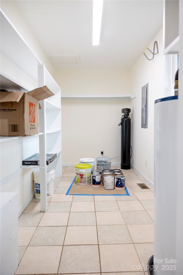 interior space with light tile patterned floors, electric panel, water heater, and attic access