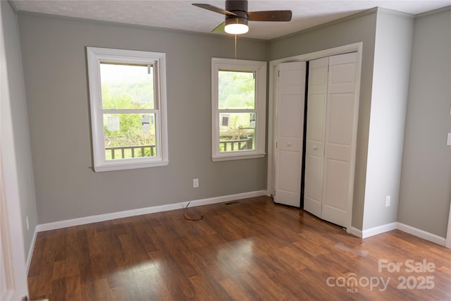 unfurnished bedroom featuring baseboards, wood finished floors, multiple windows, and a closet