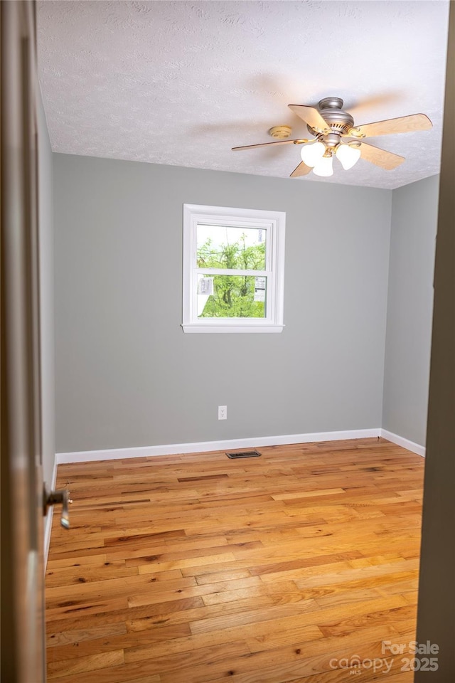 empty room with a textured ceiling, visible vents, baseboards, and light wood-style floors