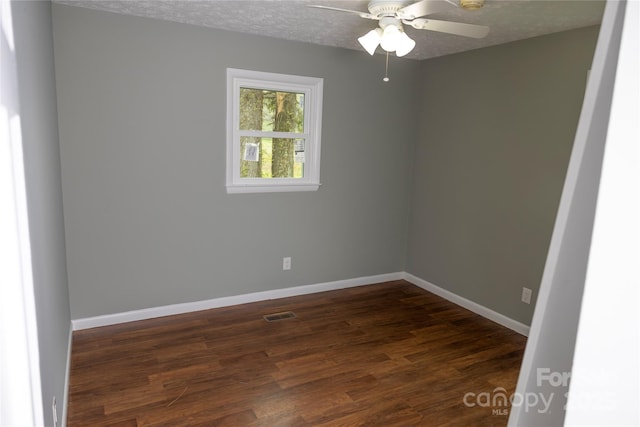 spare room with dark wood-type flooring, a ceiling fan, visible vents, and baseboards