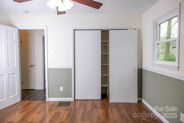 unfurnished bedroom with wood finished floors, a ceiling fan, visible vents, and a closet