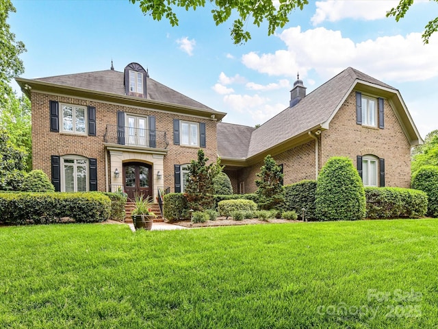 colonial-style house featuring french doors, a chimney, a front lawn, and brick siding