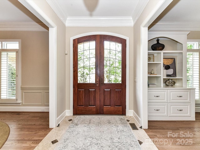 entryway featuring crown molding, baseboards, wood finished floors, and visible vents