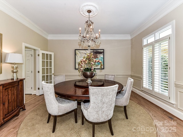 dining space with light wood-style floors, a wainscoted wall, crown molding, and a chandelier
