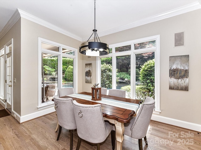 dining space featuring light wood-style floors, baseboards, crown molding, and a notable chandelier