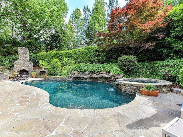 pool featuring an outdoor stone fireplace, an in ground hot tub, and a patio