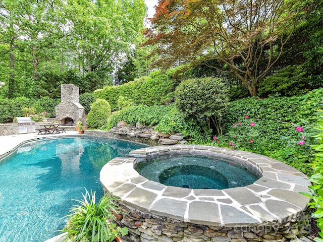 outdoor pool featuring an in ground hot tub, a patio area, and an outdoor stone fireplace