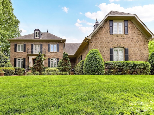colonial home with brick siding, a front lawn, a balcony, and a chimney