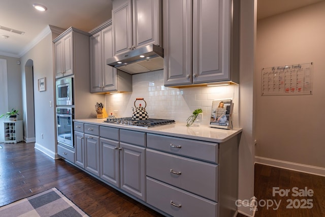 16711 Monocacy Blvd, Huntersville, NC 28078 - kitchen with under cabinet range hood, crown molding, gray cabinetry, arched walkways, and appliances with stainless steel finishes
