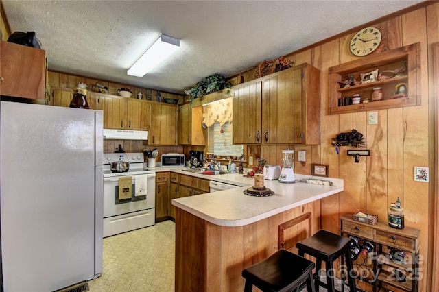 134 Raven Rdg, Maggie Valley, NC 28751 - kitchen featuring white appliances, under cabinet range hood, a peninsula, brown cabinetry, and light countertops