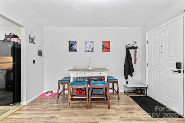 dining area with light wood-type flooring, a textured ceiling, and baseboards