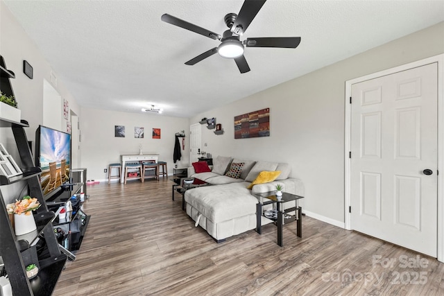 living area with baseboards, a textured ceiling, ceiling fan, and wood finished floors