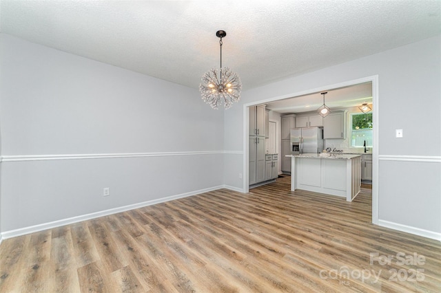 interior space with light wood-style floors, baseboards, a textured ceiling, and a chandelier