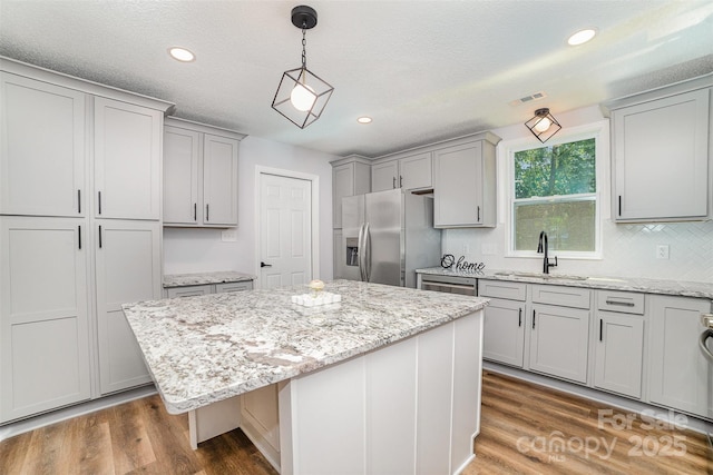 kitchen featuring gray cabinets, a center island, a sink, light stone counters, and stainless steel appliances