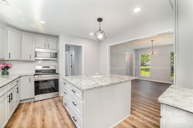 kitchen with decorative backsplash, light wood finished floors, hanging light fixtures, and stainless steel appliances