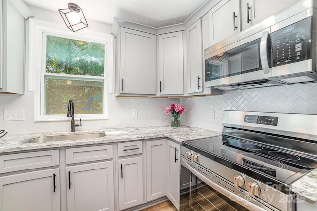 kitchen featuring backsplash, light stone countertops, a sink, light wood finished floors, and stainless steel appliances