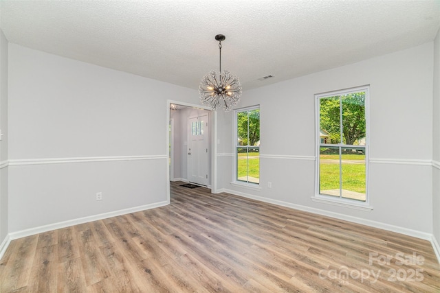 empty room with baseboards, a notable chandelier, a healthy amount of sunlight, and wood finished floors