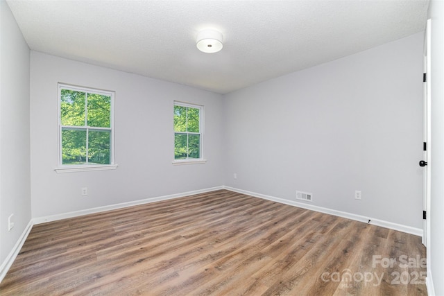 unfurnished room featuring baseboards, wood finished floors, and visible vents