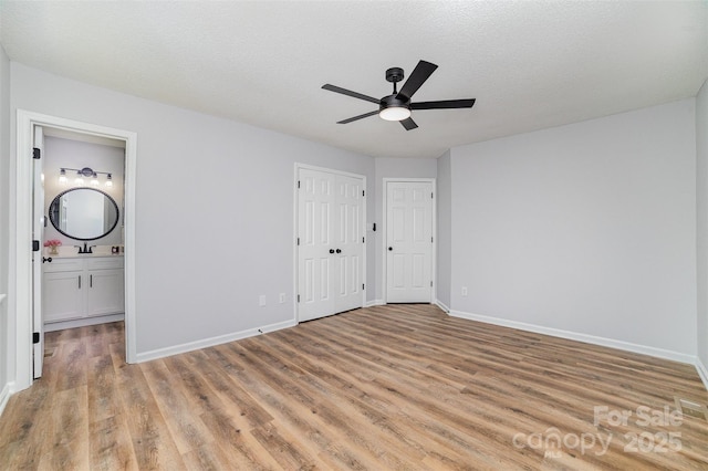unfurnished bedroom featuring baseboards, ceiling fan, light wood-type flooring, a textured ceiling, and ensuite bath